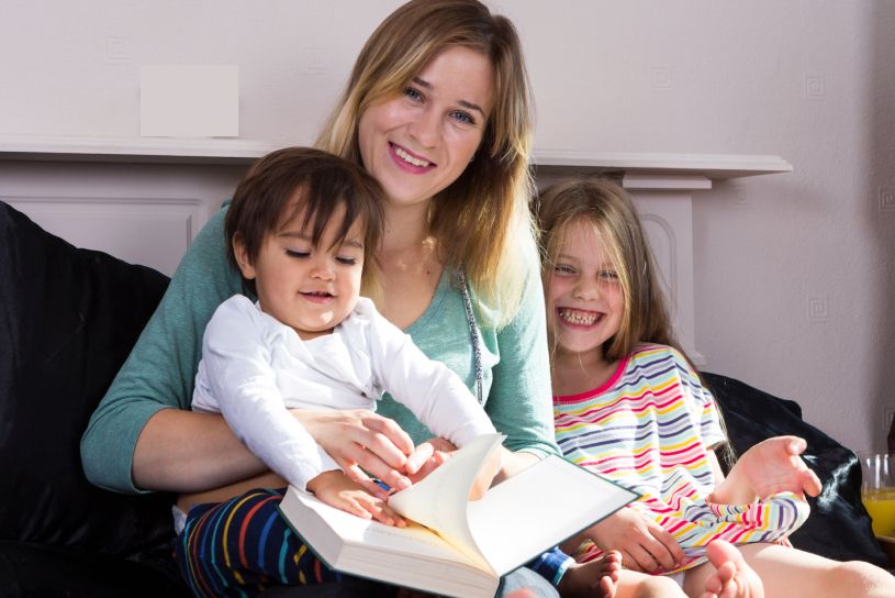 Woman reading a self-help book with two children on her lap