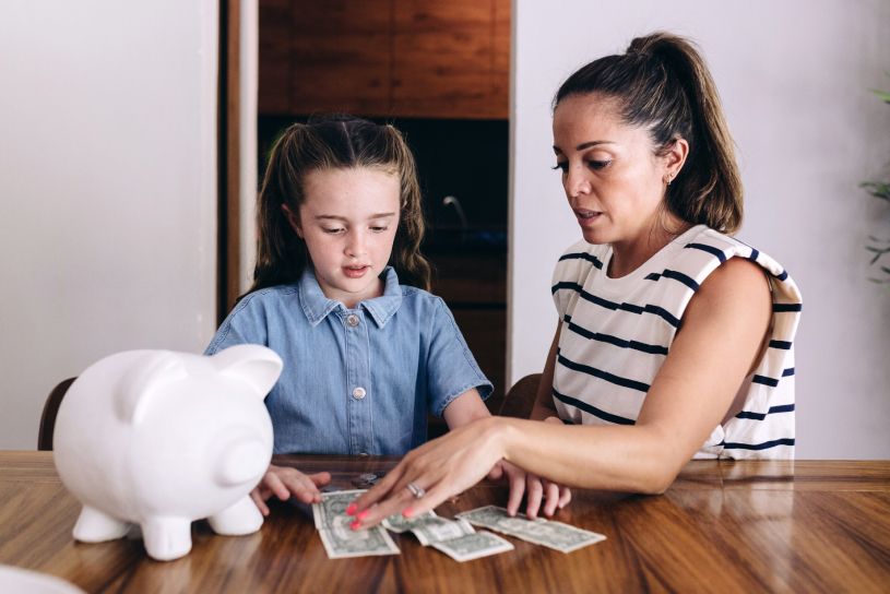 Mother teaching young daughter about saving money at kitchen table