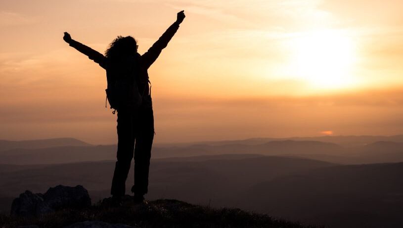 Woman celebrating at the top of a cliff on a hike at sunset